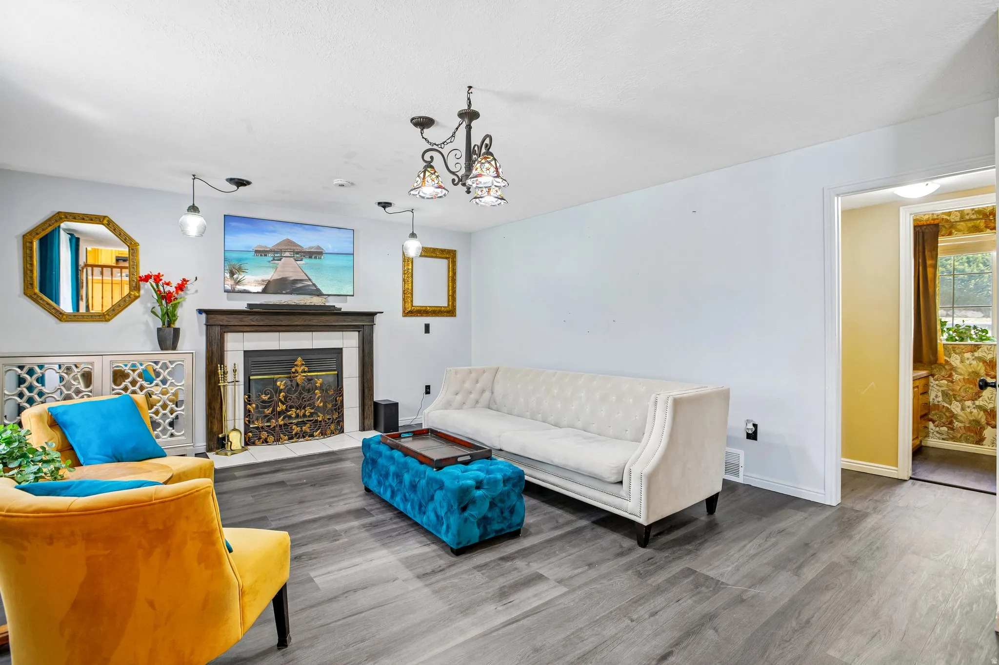 Living space featuring wood-finish flooring, a fireplace with a decorative screen and a dark wood mantel, and a multi-arm chandelier