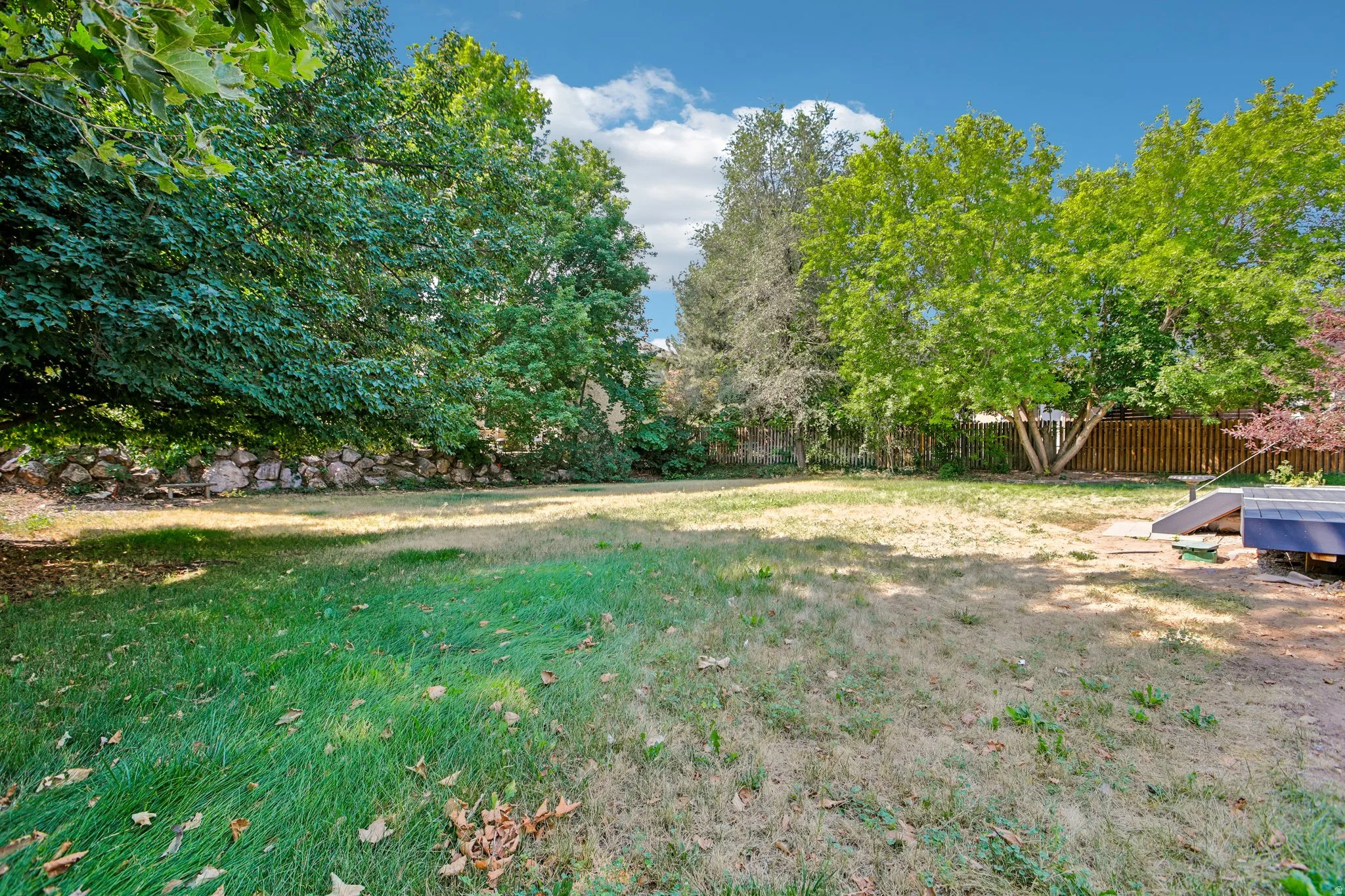 Expansive grassy yard with mature trees and a stone retaining wall