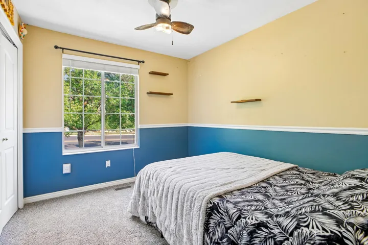 Window with horizontal blinds, overhead ceiling fan with light, wall-mounted shelving, and carpeted flooring