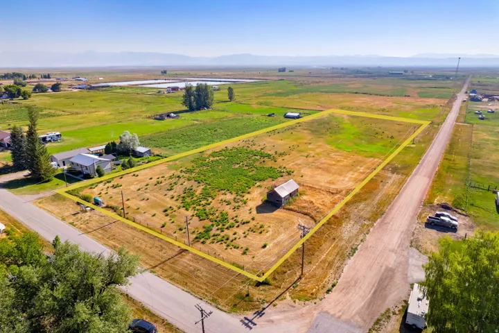 Expansive lot featuring a single structure, surrounding green fields, and distant mountains