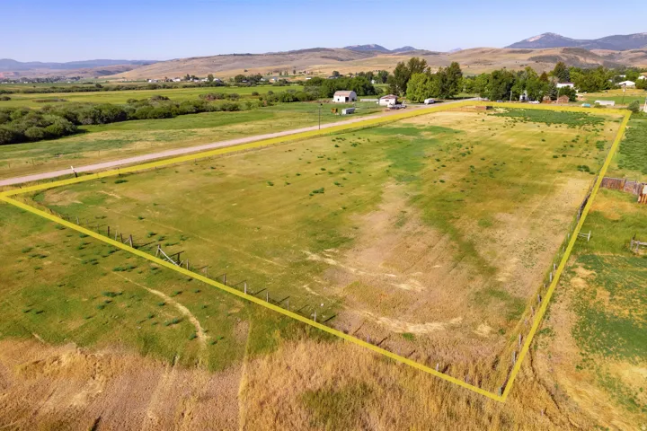 Expansive parcel featuring a perimeter fence and varied topography, with a paved road bordering one side and distant mountains framing the background