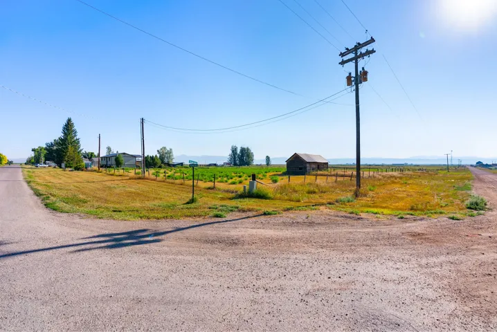 Gravel road frontage, expansive land parcel, mature trees, open field, and distant mountain range