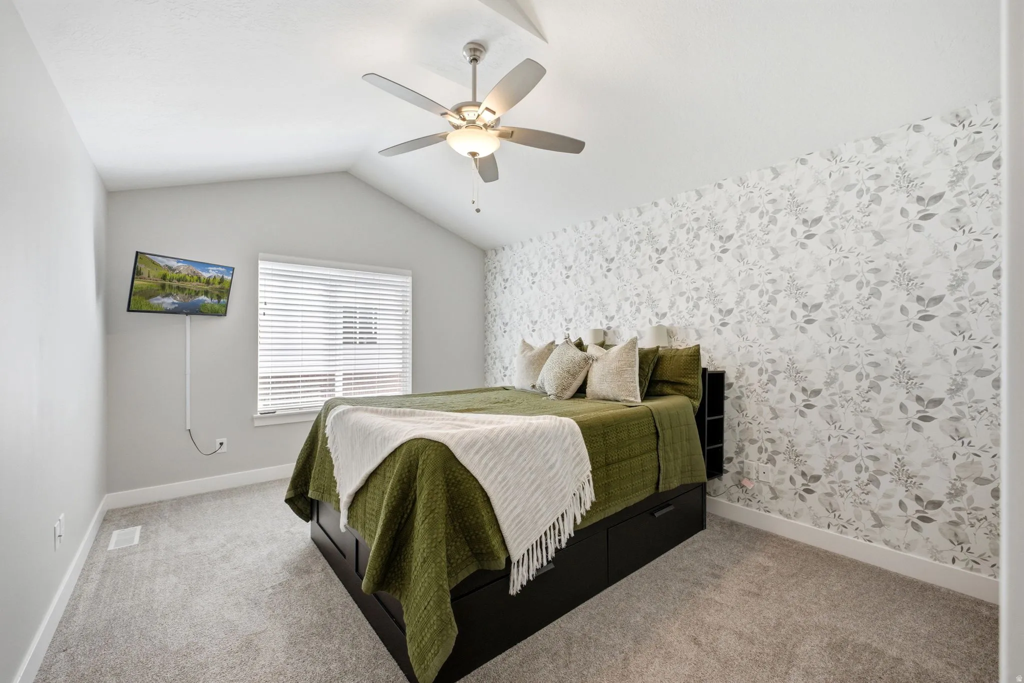 Vaulted ceiling with ceiling fan, wall-mounted television, patterned accent wall, and window with blinds