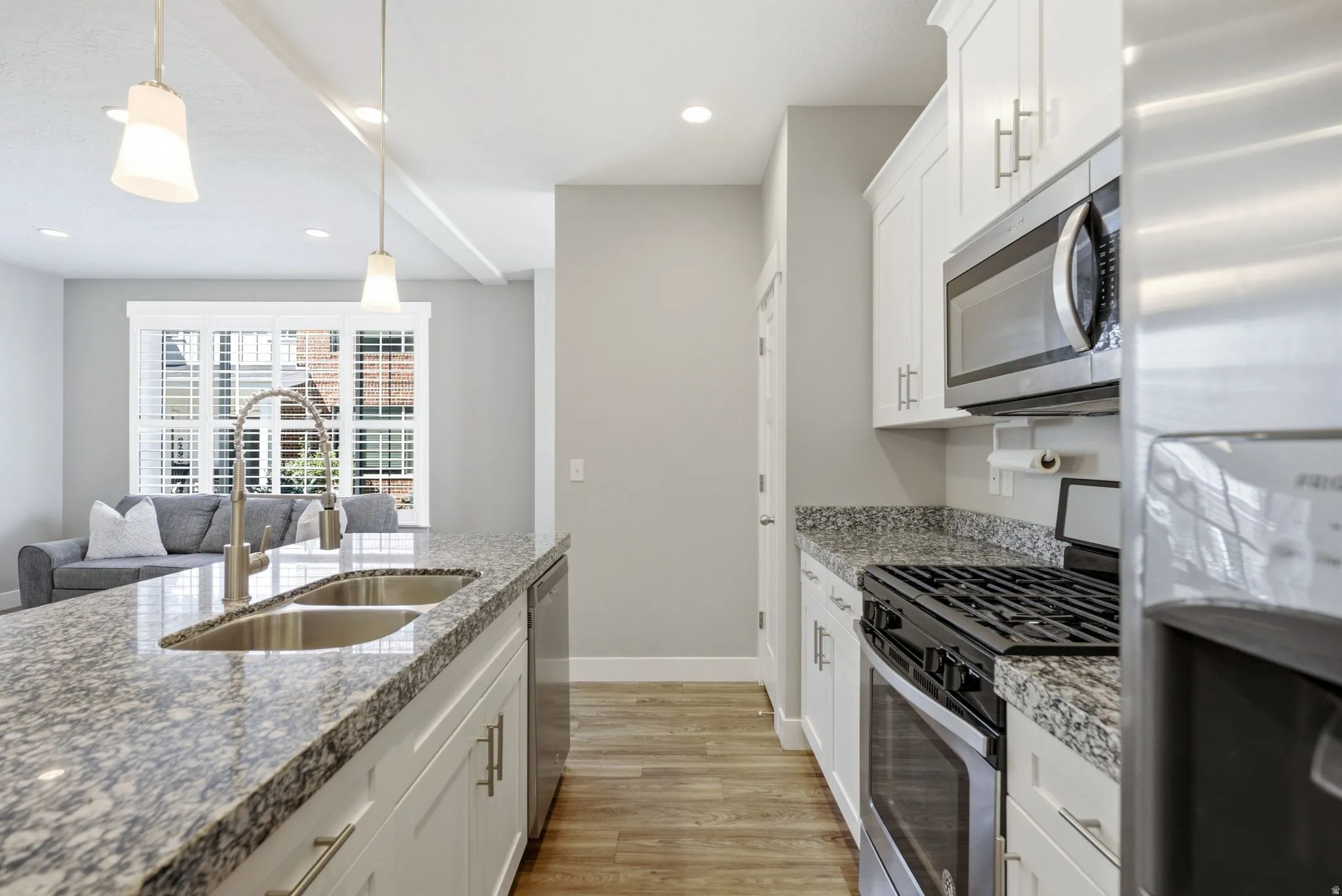 Kitchen featuring light wood-finish flooring, white cabinetry, granite countertops, stainless steel appliances, and a double basin sink with a gooseneck faucet