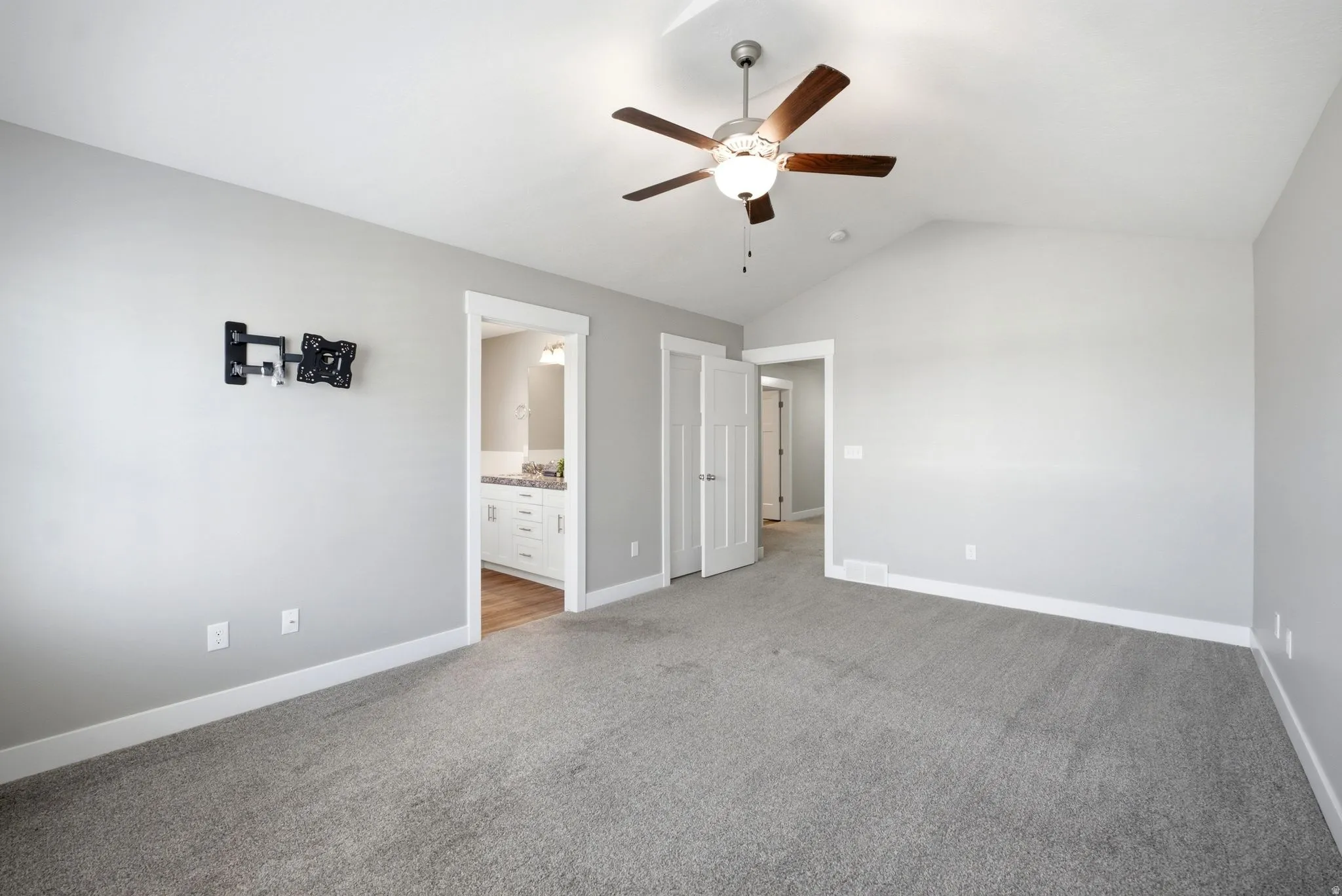 Spacious bedroom featuring neutral gray carpeting, soft ambient lighting from a ceiling fan with integrated fixture, and multiple closet access points