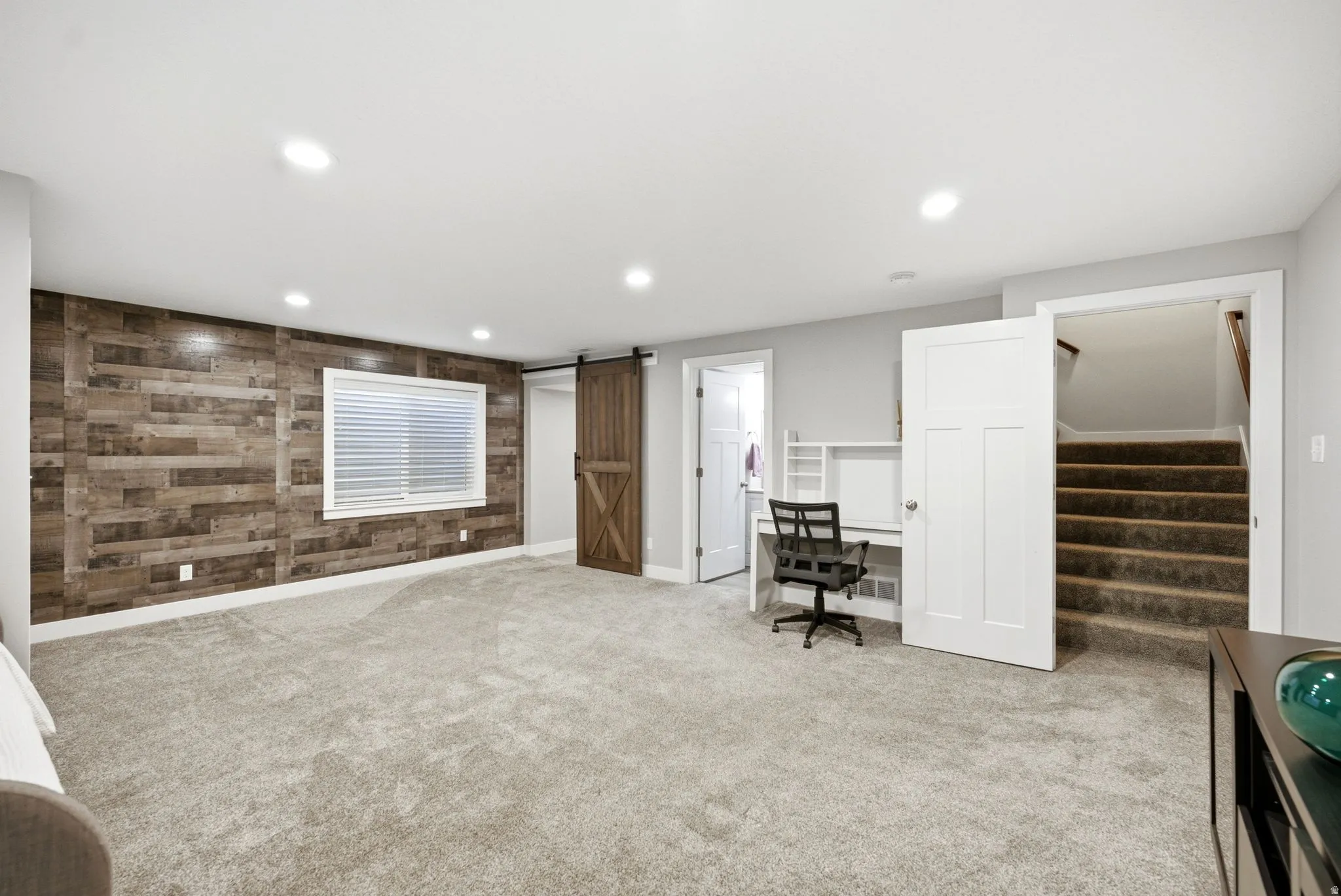 Recessed lighting illuminates a spacious room featuring a wood-panel accent wall and light-colored carpeting