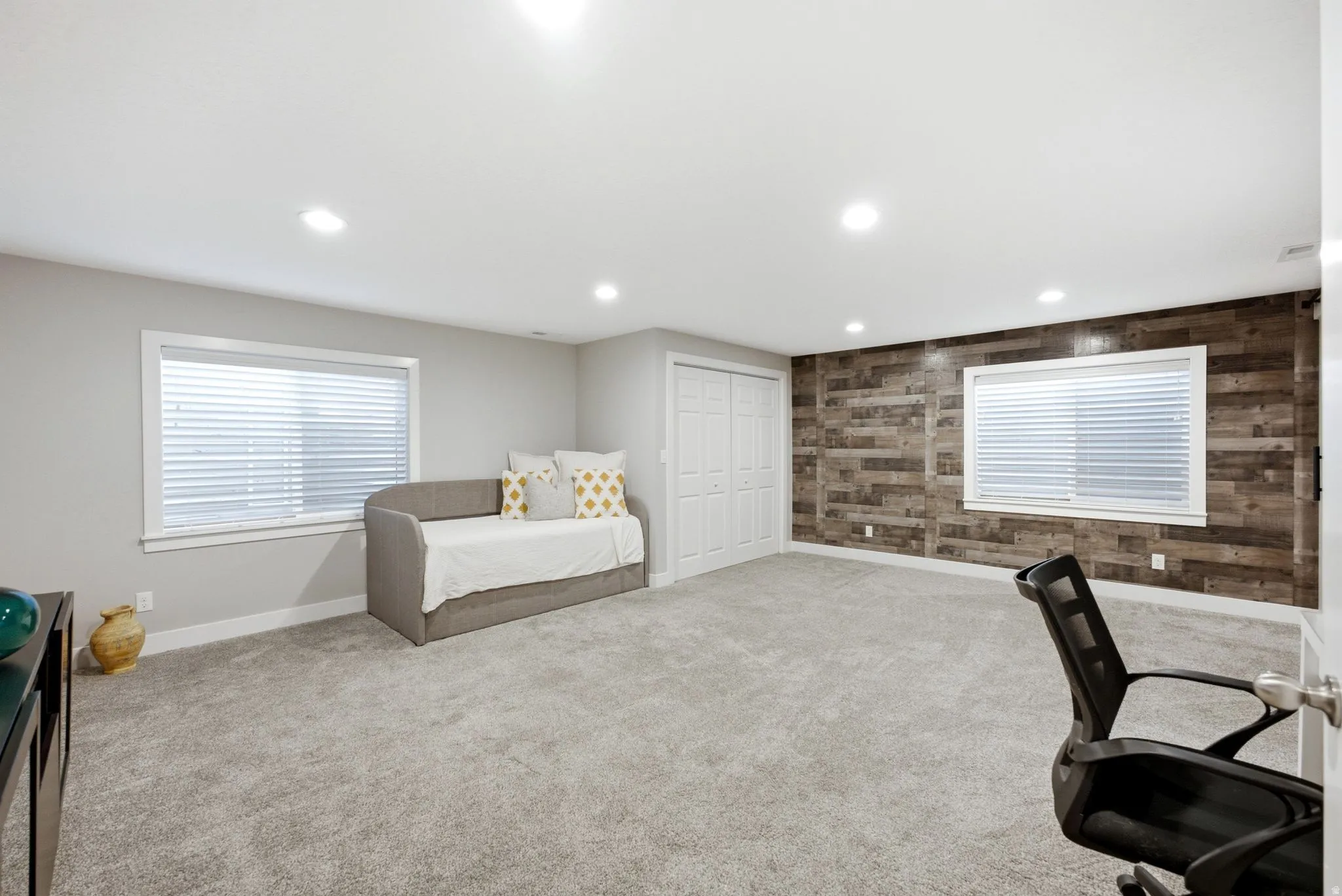 Recessed lighting, light gray wall paint, wood-finish accent wall, white-framed windows, and a double-door closet