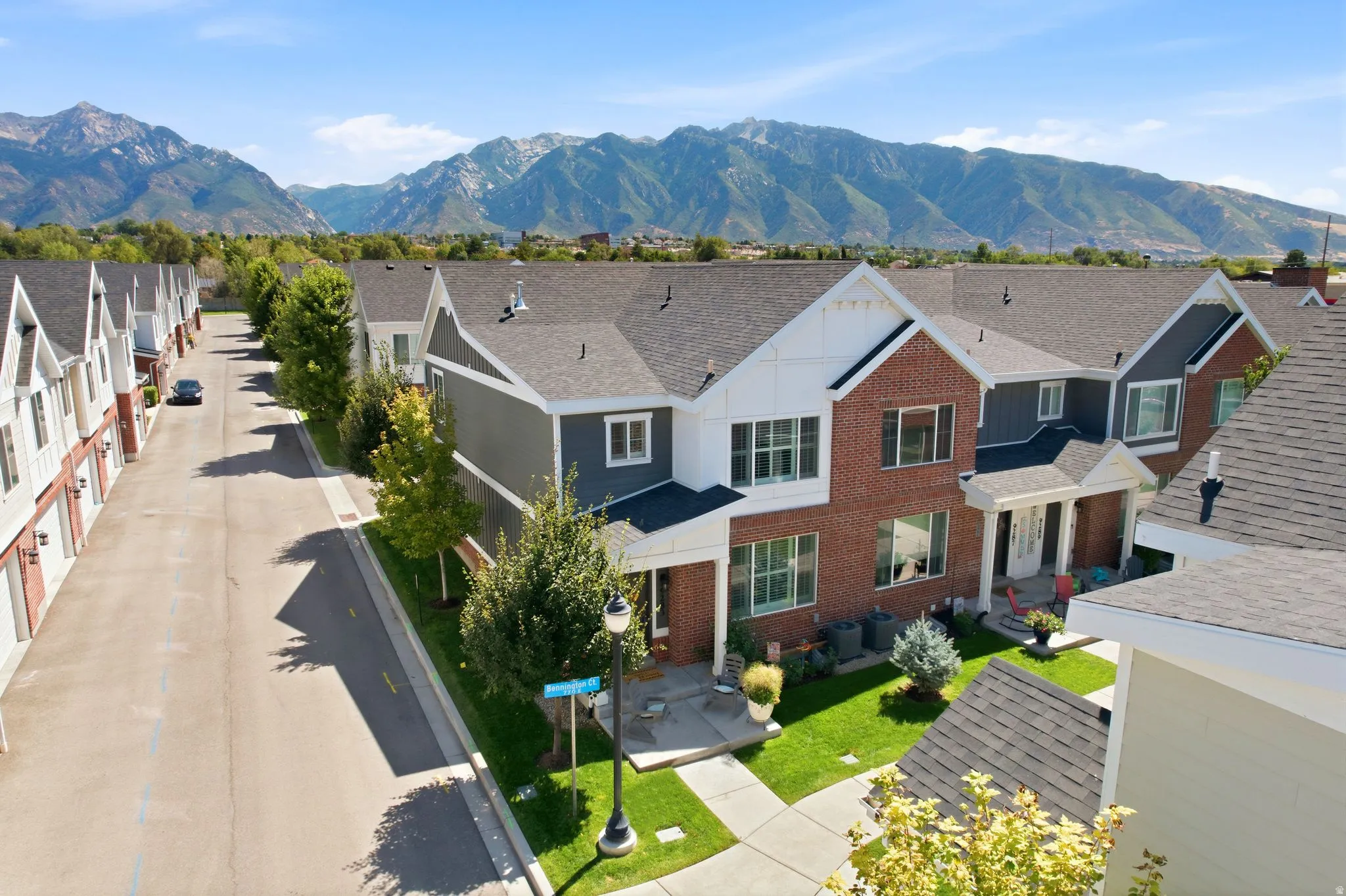 Two-story townhome featuring brick and siding facade, a covered entry, and mature landscaping