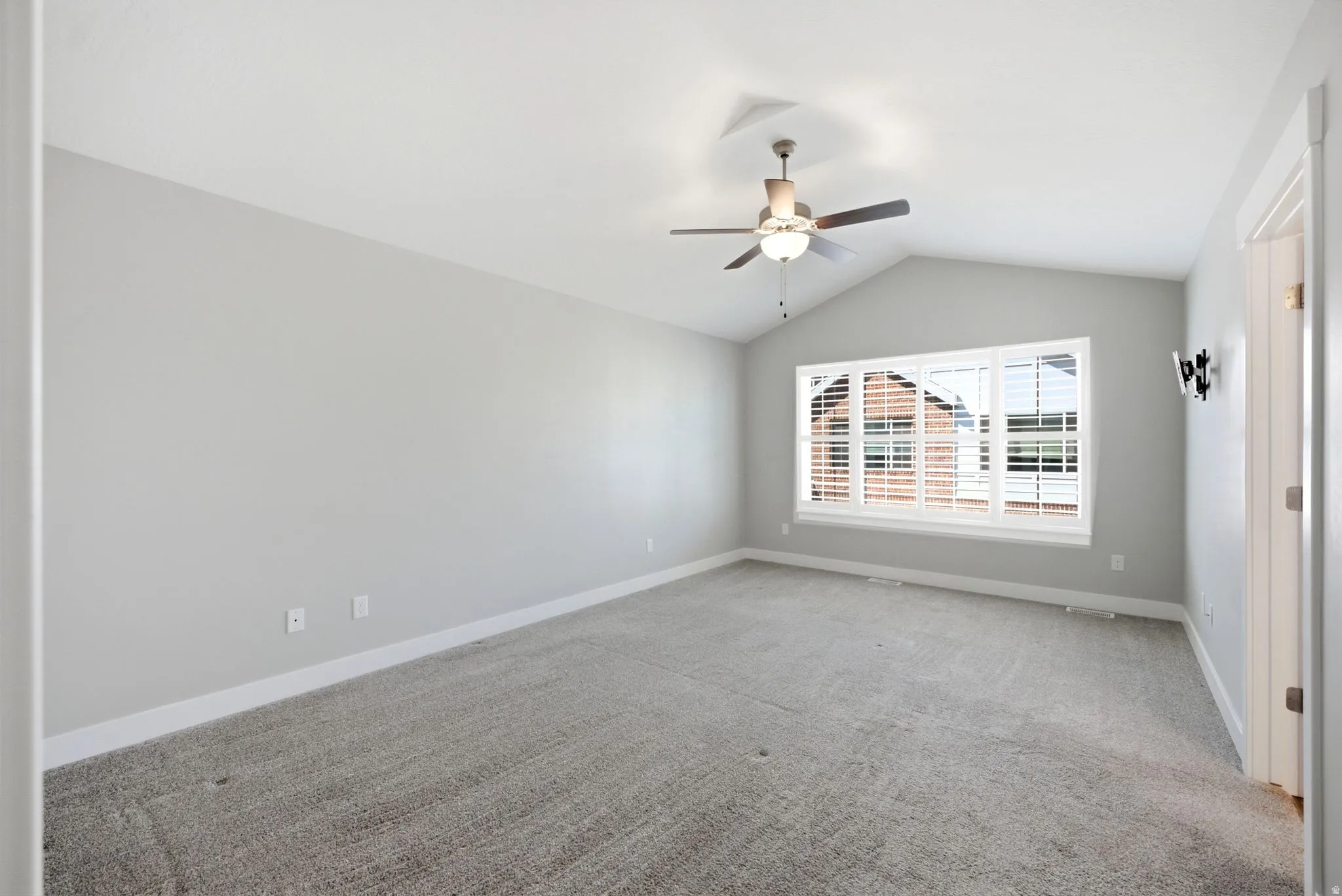 Vaulted ceiling with a ceiling fan, carpeted flooring, and a multi-pane window with plantation shutters