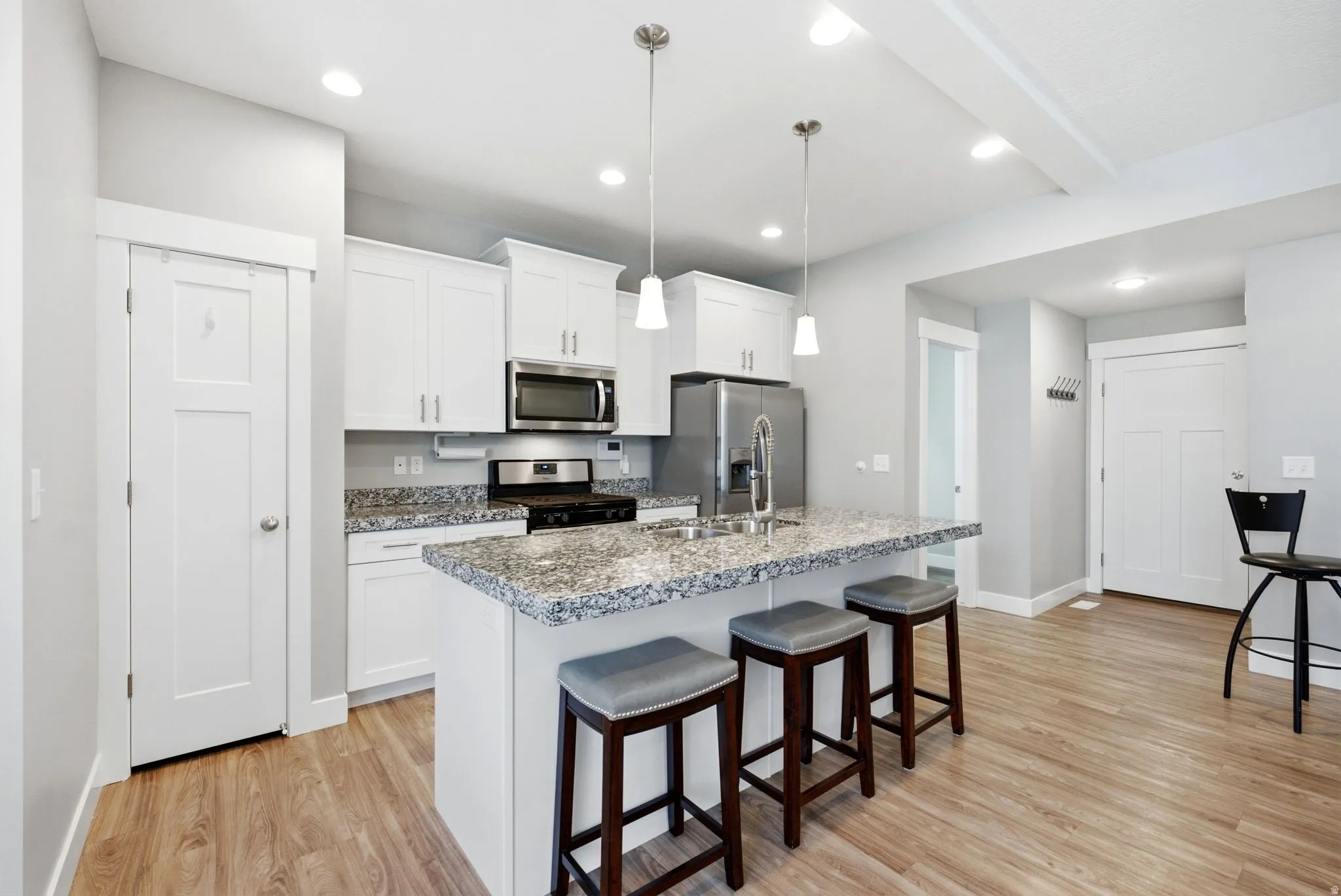 White shaker cabinetry, stainless steel appliances, granite countertops, wood-finish flooring, and recessed lighting