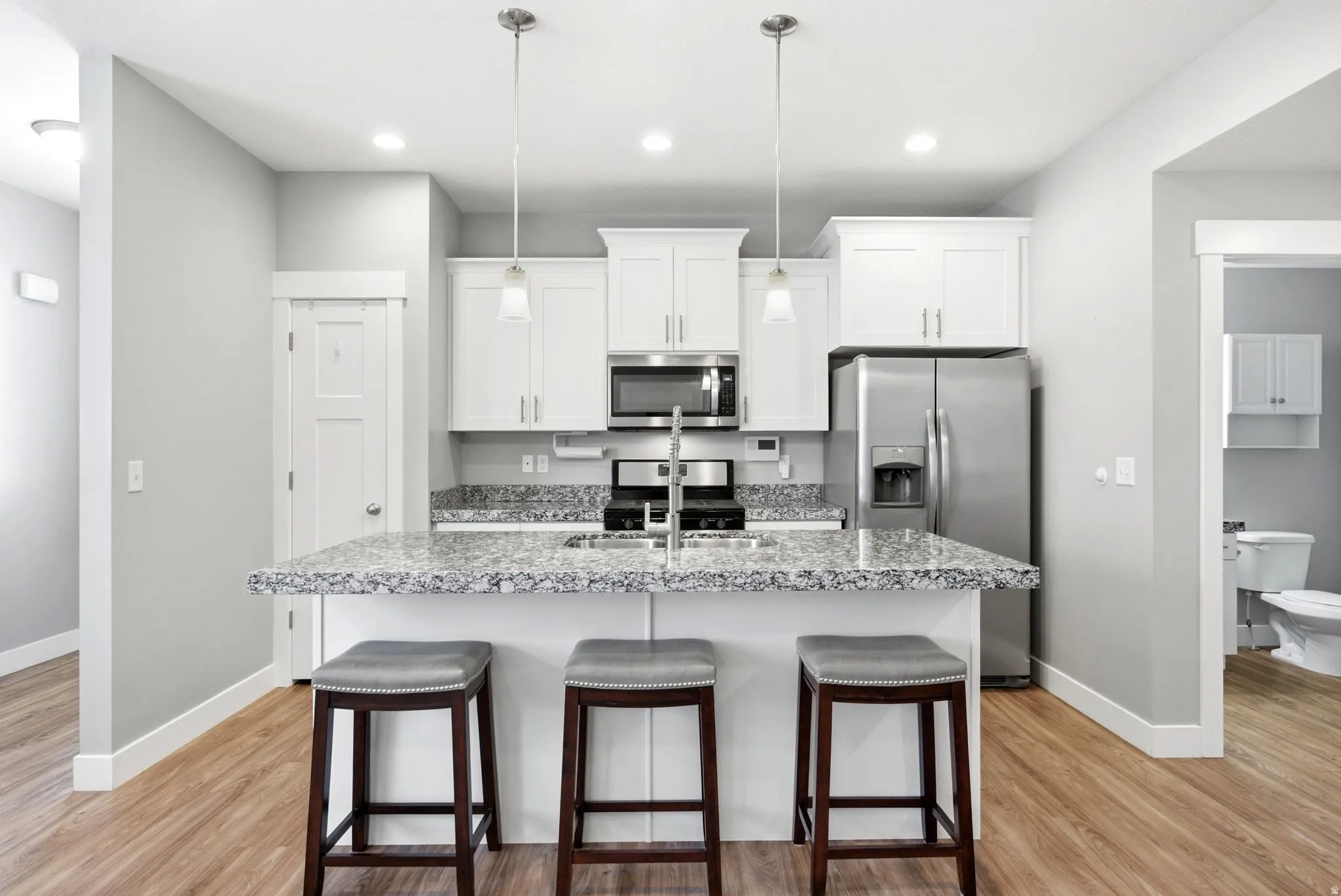 Kitchen featuring white cabinetry, stainless steel appliances, a center island with pendant lighting, and wood-finish flooring
