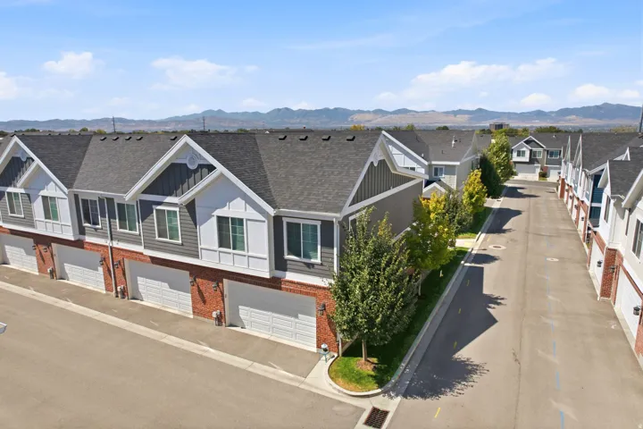 Townhome exterior with brick and horizontal siding, individual garage doors, and a paved street with mature trees
