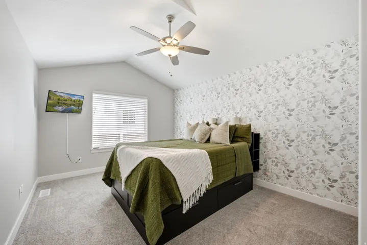 Vaulted ceiling with ceiling fan, wall-mounted television, patterned accent wall, and window with blinds