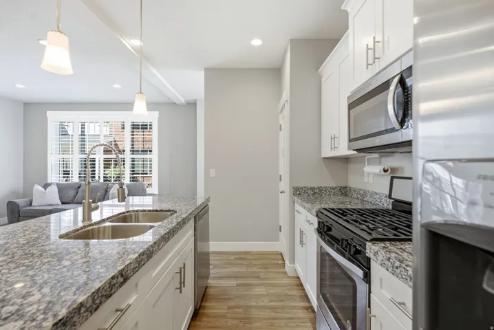 Kitchen featuring light wood-finish flooring, white cabinetry, granite countertops, stainless steel appliances, and a double basin sink with a gooseneck faucet