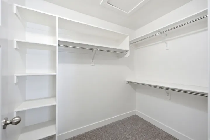 Built-in white shelving, multiple hanging rods, and gray carpeting
