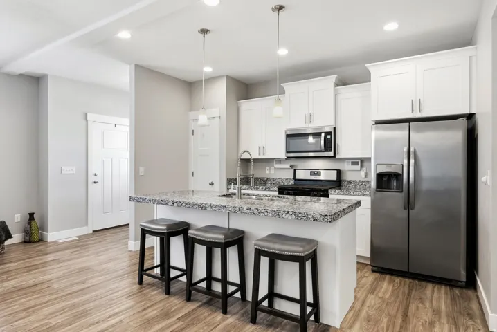 Kitchen featuring an island with stone countertop, stainless steel appliances, white cabinetry, and wood-finish flooring