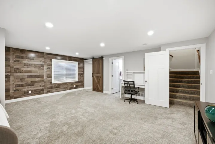 Recessed lighting illuminates a spacious room featuring a wood-panel accent wall and light-colored carpeting