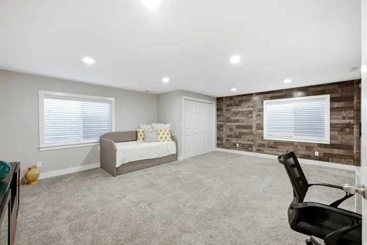 Recessed lighting, light gray wall paint, wood-finish accent wall, white-framed windows, and a double-door closet