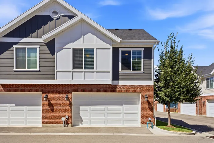 Exterior featuring multi-toned siding, brick detailing, white window trim, and white garage doors