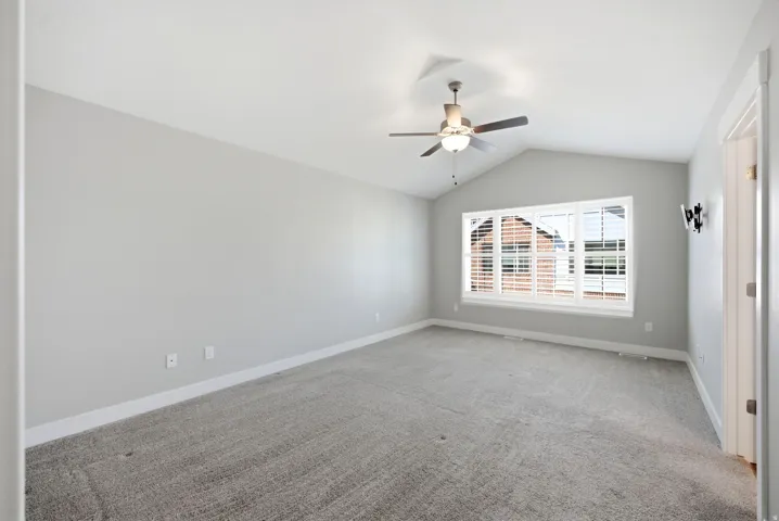 Vaulted ceiling with a ceiling fan, carpeted flooring, and a multi-pane window with plantation shutters