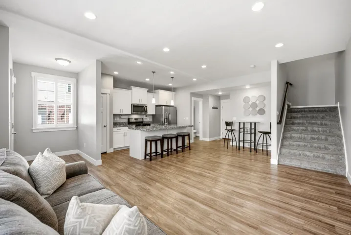 Open-concept living area featuring wood-finish flooring, recessed lighting, a kitchen island with seating, white cabinetry, and stainless steel appliances