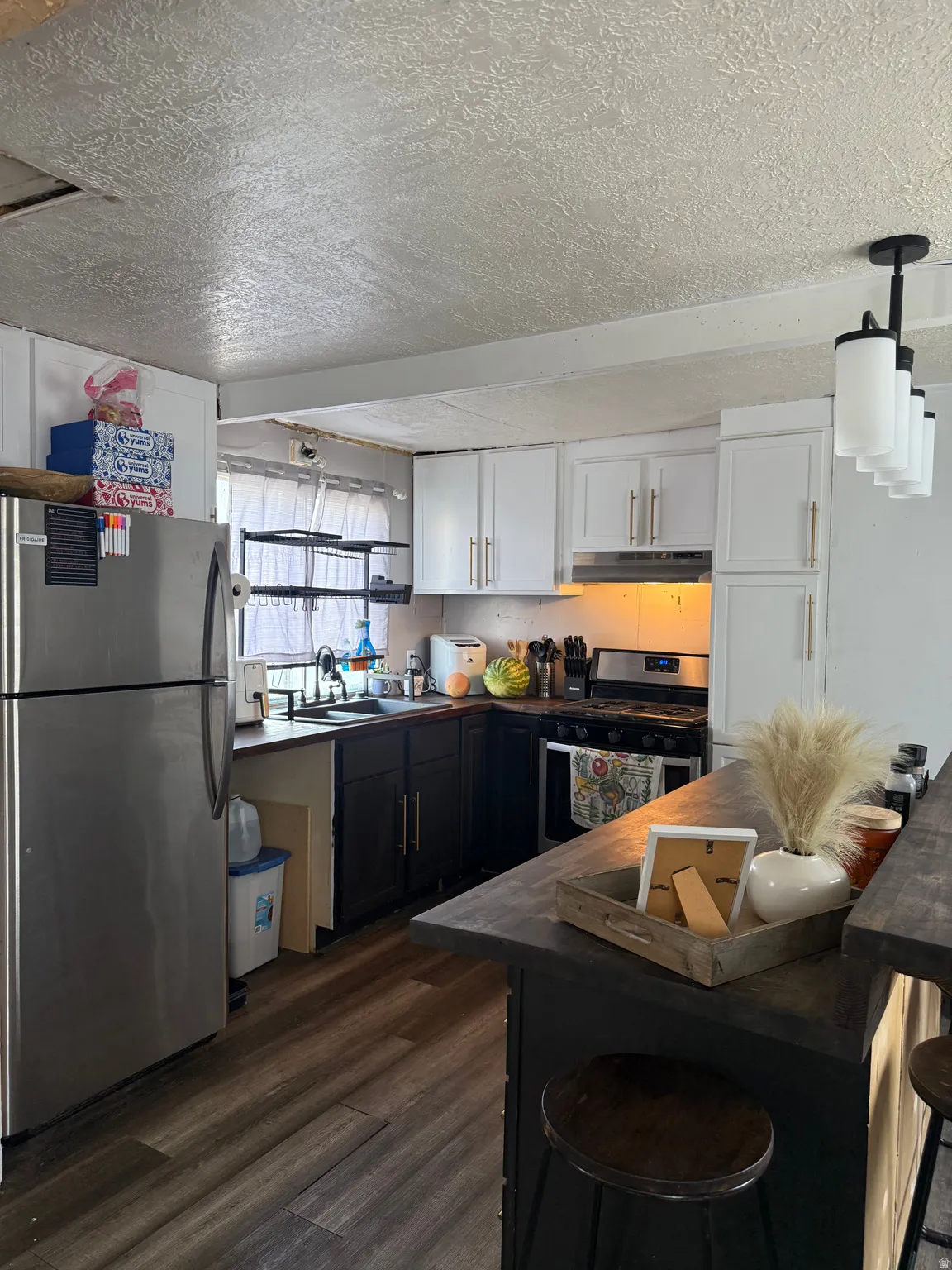 Modern kitchen featuring stainless steel appliances, dark wood-finish flooring, two-tone cabinetry, and a black multi-light pendant fixture