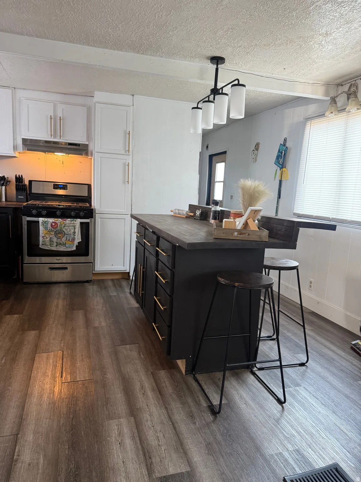 Kitchen featuring wood-finish flooring, stainless steel range, white upper cabinetry, and a dark kitchen island with gold-tone hardware