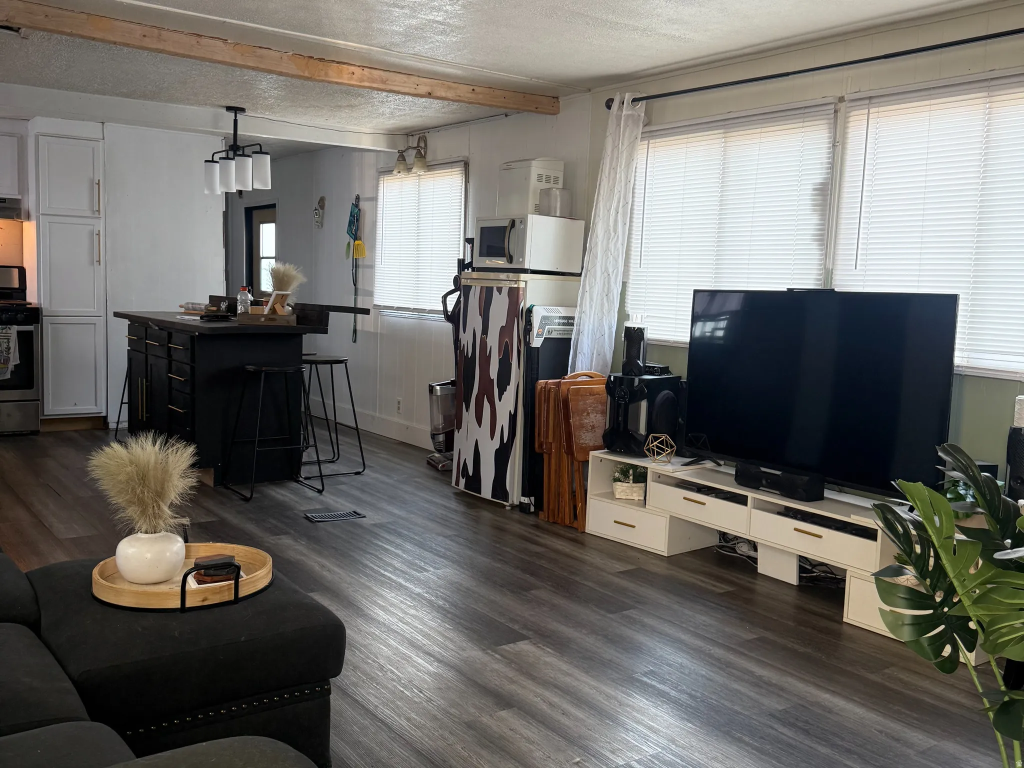 Open-concept living space with wood-finish flooring, a kitchen island with seating, a modern chandelier, and multiple windows with blinds