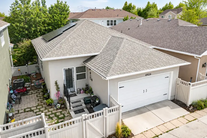 Stucco exterior with a pitched shingle roof, integrated solar panels, an attached garage, and a fenced side yard with paver stones
