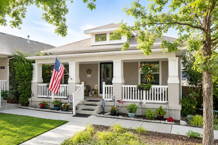 Covered front porch with white railings and columns, dormer window, and an established front yard with concrete pathways