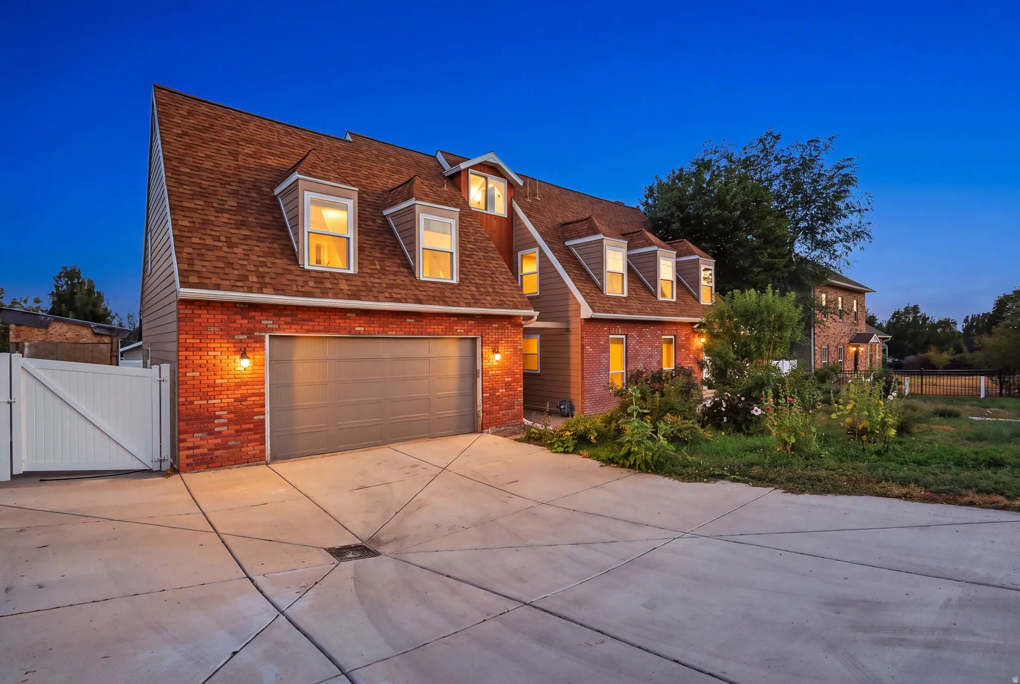 Brick facade with siding accents, attached garage, multiple dormer windows, and a paved driveway