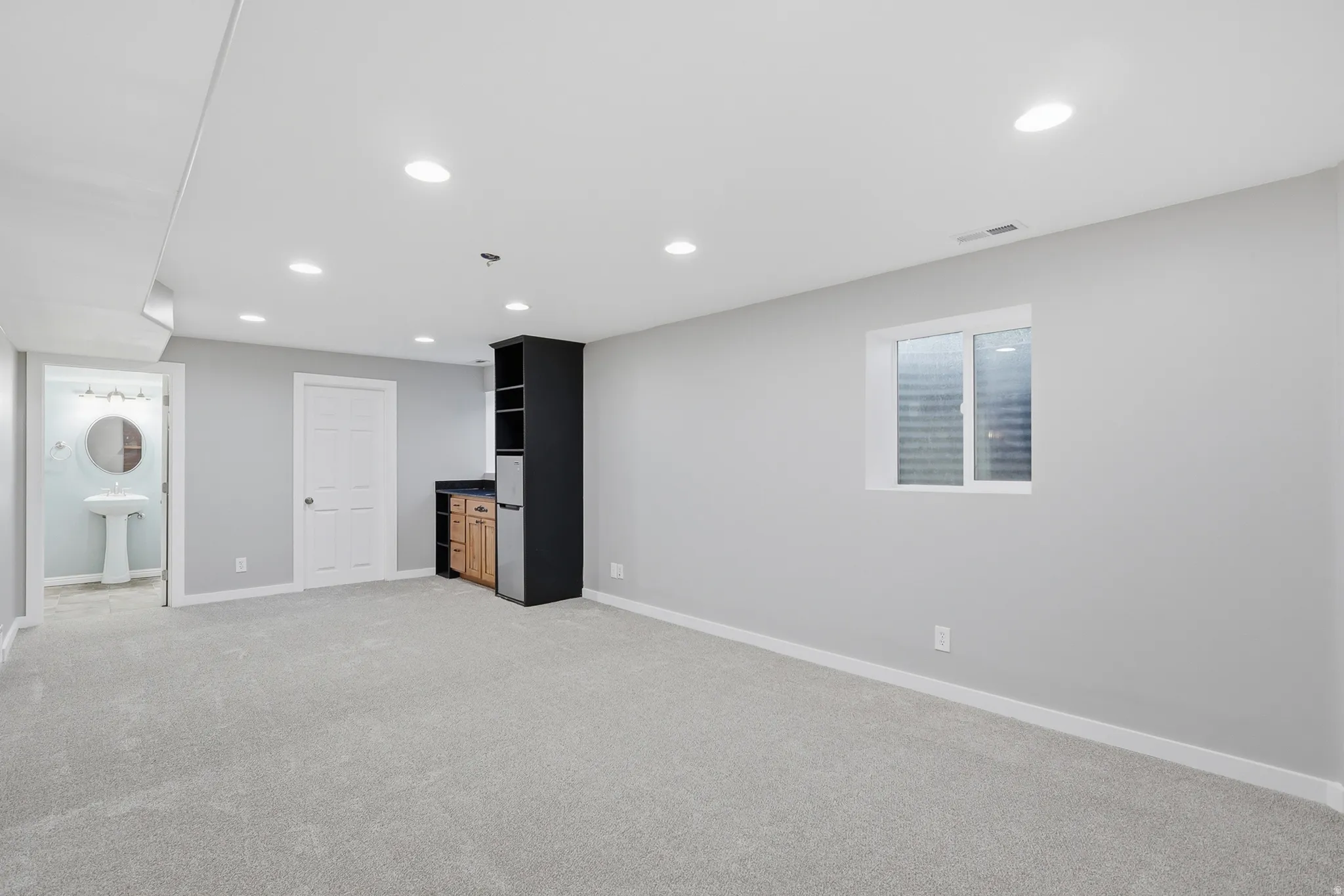 Recessed lighting, light gray carpet, and a built-in wet bar with wood-finish cabinetry