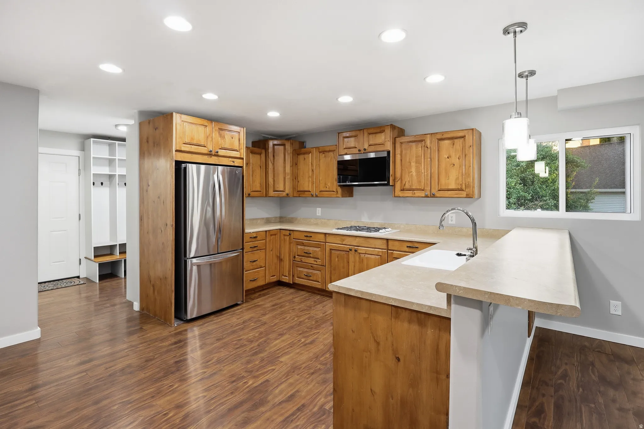 Kitchen featuring wood-finish cabinetry, stainless steel appliances, a breakfast bar, recessed lighting, and wood-finish flooring