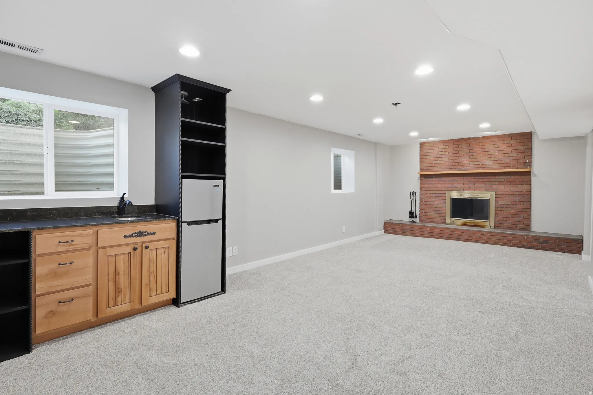 Built-in wet bar with wood cabinetry and dark countertop, brick fireplace with mantel, recessed lighting, and light-colored carpeting