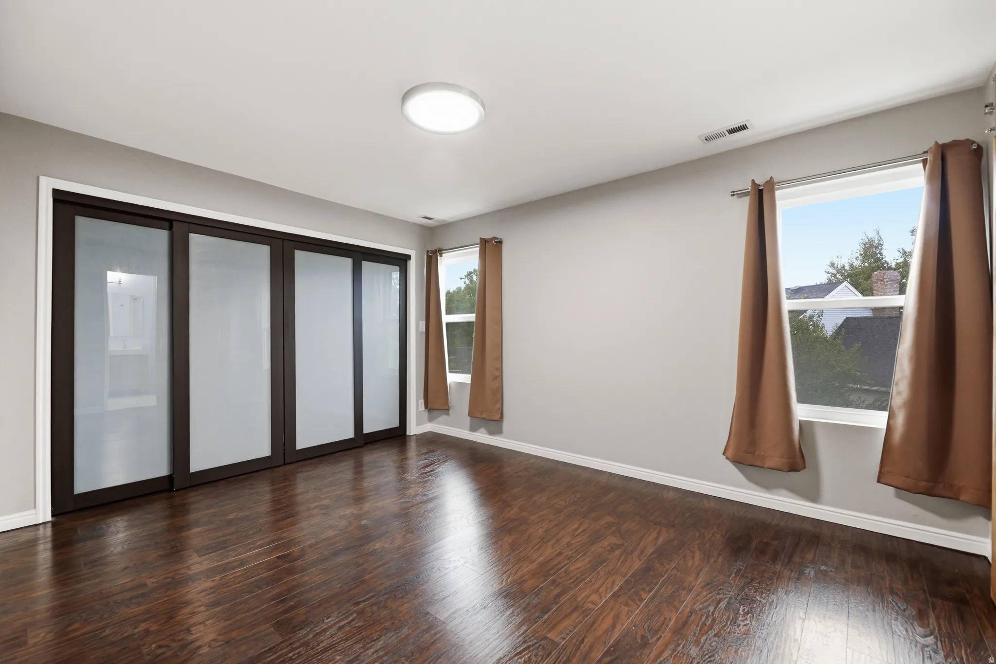 Wood-finish flooring with a satin sheen, contemporary ceiling light fixture, and dark-framed sliding doors with frosted panels