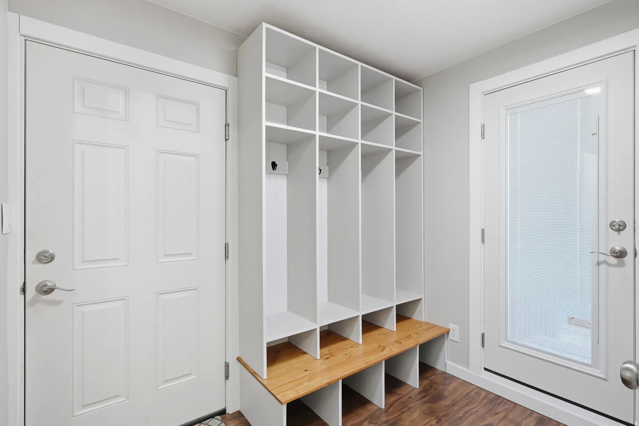 Built-in storage cubbies with wood-finish bench seating, wood-finish flooring, and two white entry doors