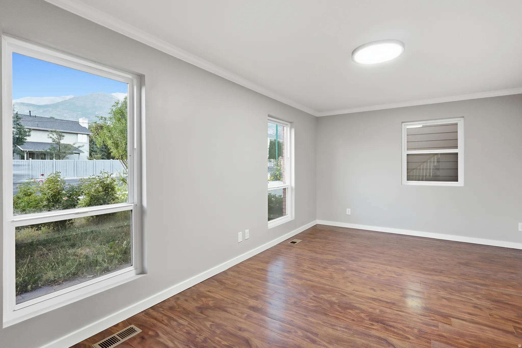 Wood-finish flooring with white trim, multiple windows, and a flush-mount ceiling light