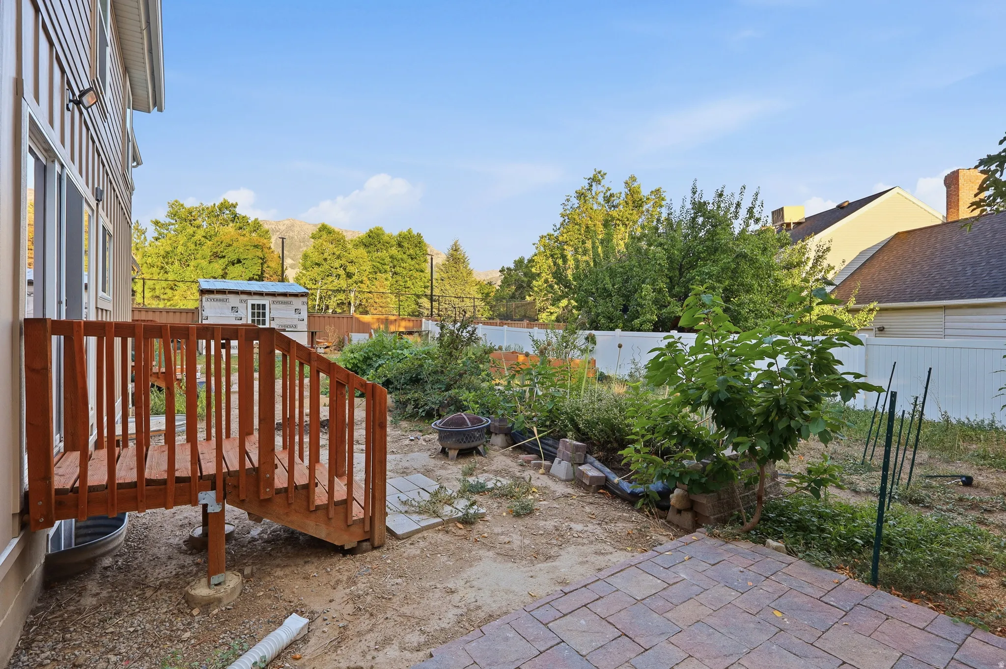 Outdoor area featuring a wood deck, paver patio, partial privacy fencing, and garden space