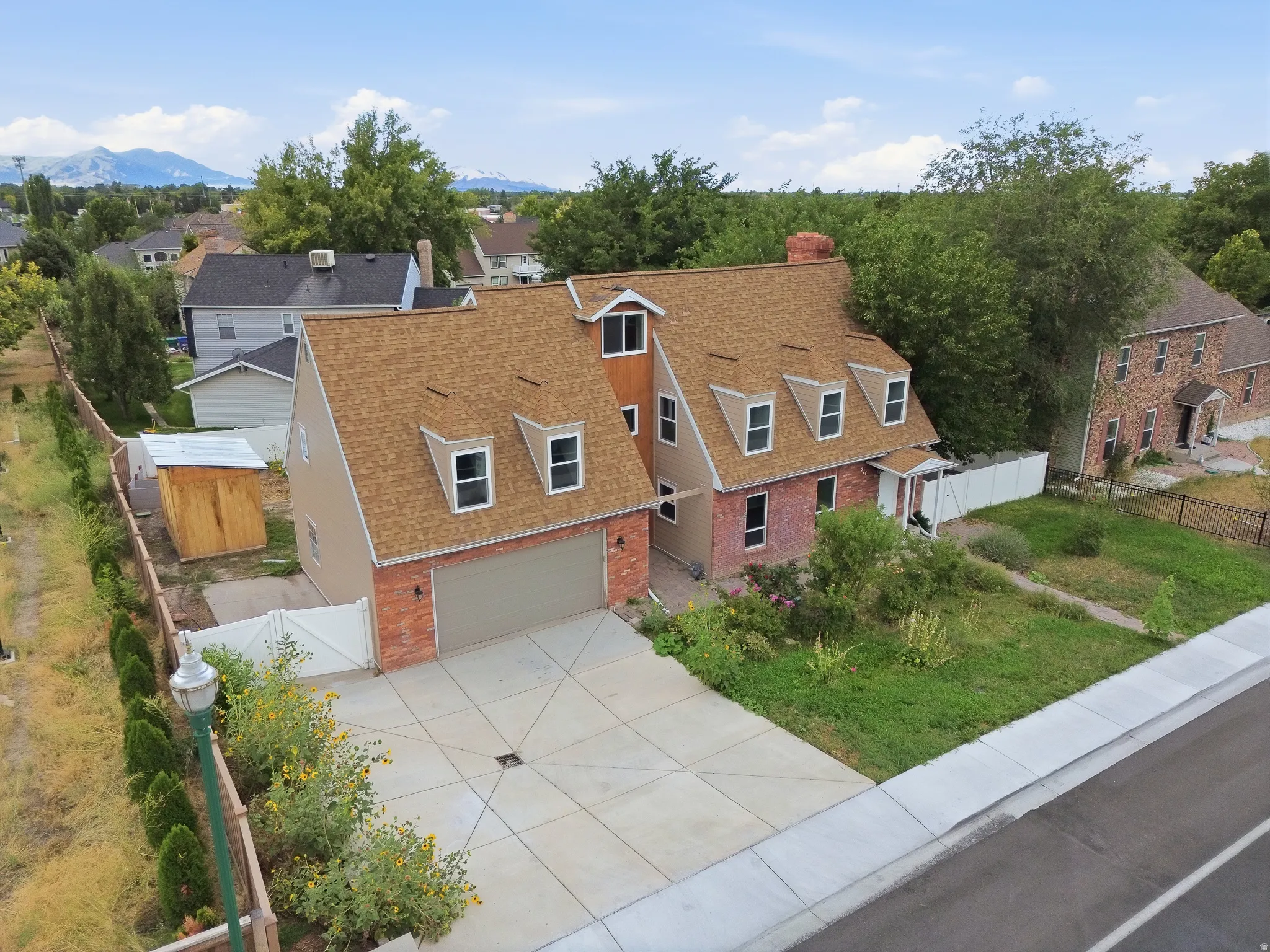Brick and siding exterior, multi-dormer roofline, attached two-car garage, concrete driveway, and white picket fencing