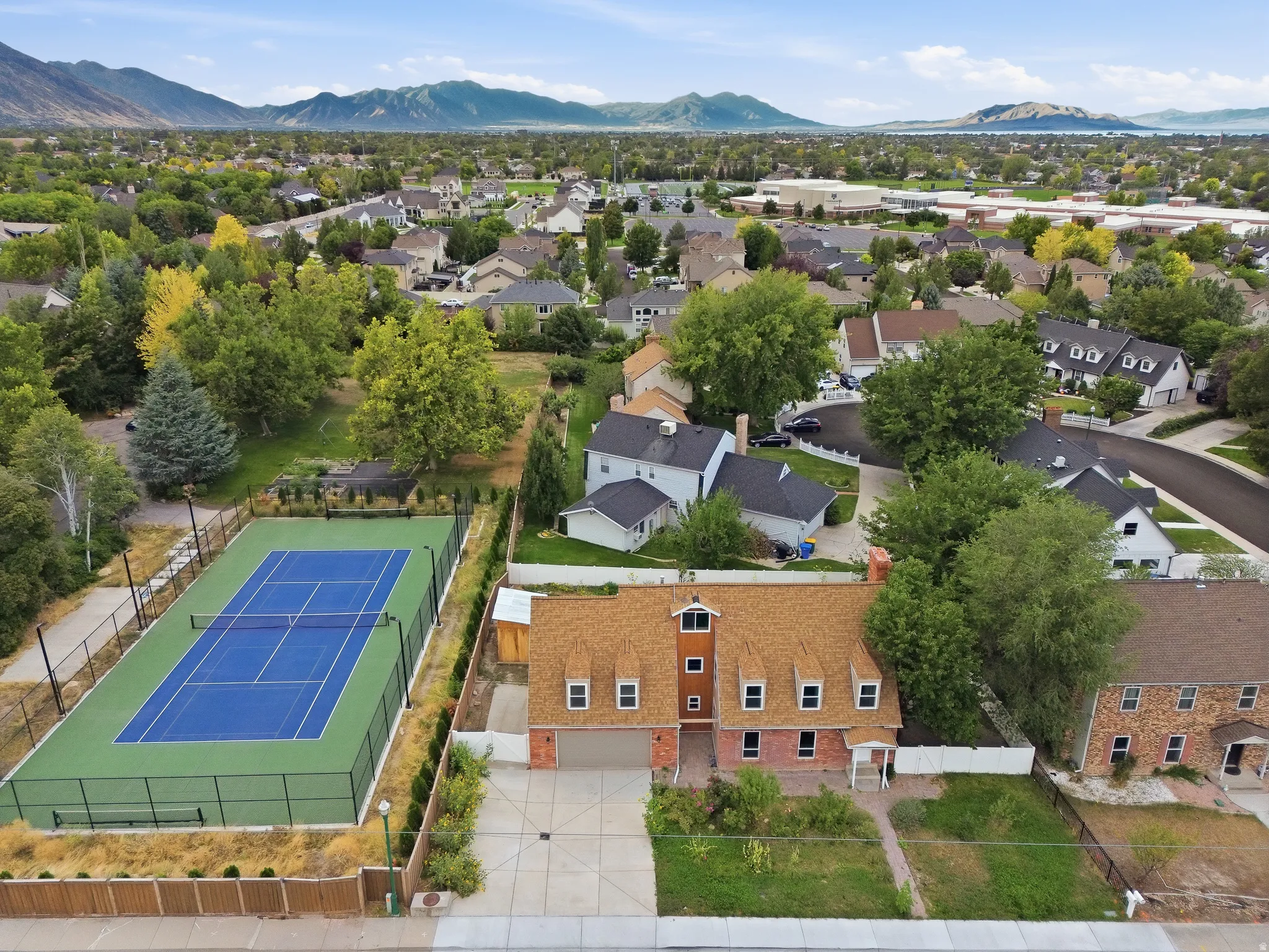 Brick exterior residence with dormer windows, attached garage, private tennis court, and mature landscaping