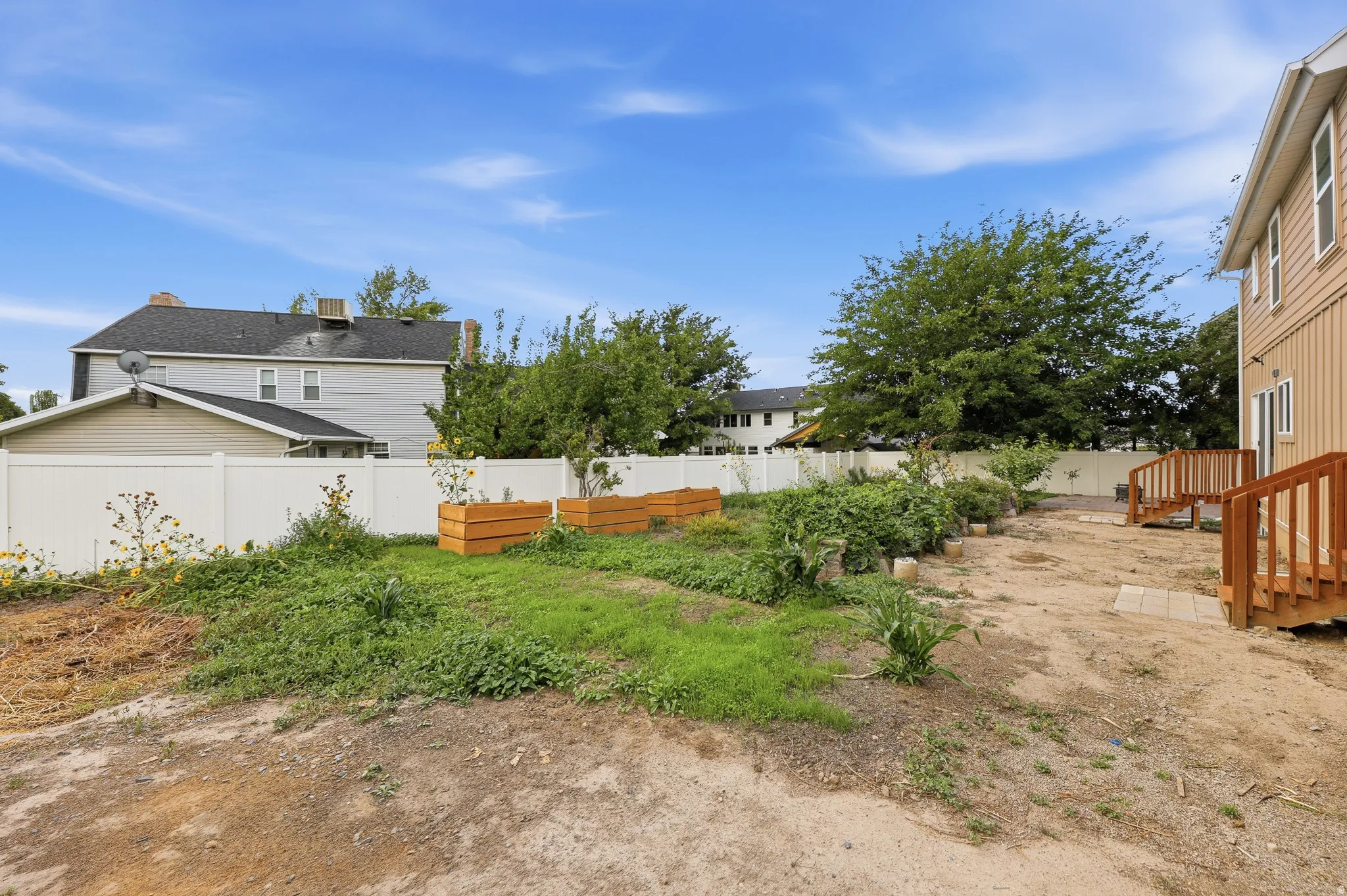 Spacious backyard featuring wood-finish deck access, raised garden beds, and white vinyl perimeter fencing