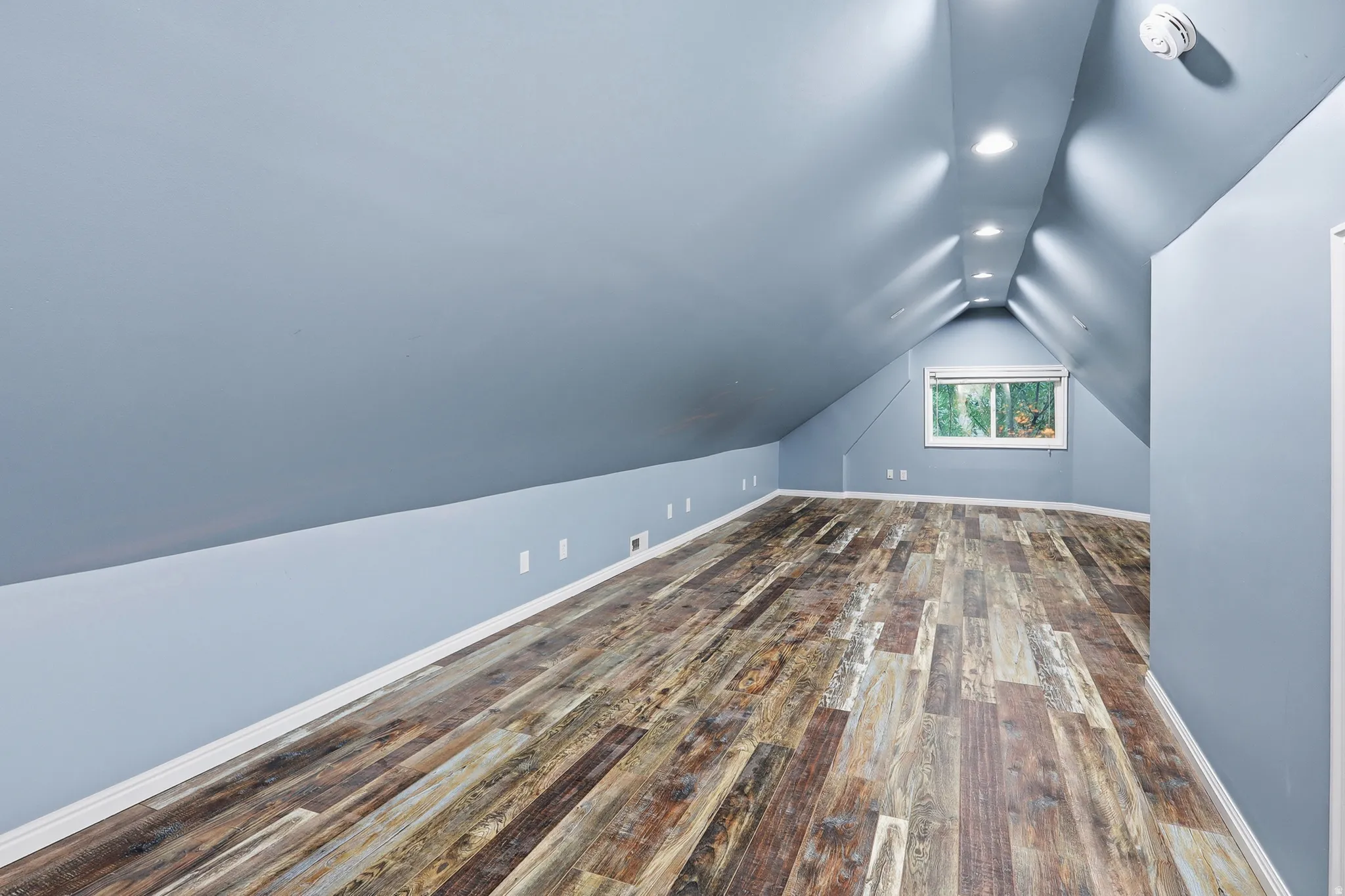 Vaulted ceiling with recessed lighting, wood-finish flooring, and a window providing natural illumination