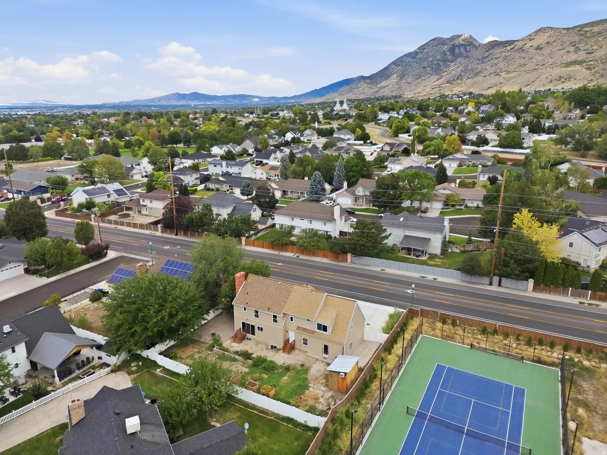 Aerial perspective of a neighborhood featuring a tennis court, residential properties, and distant mountains