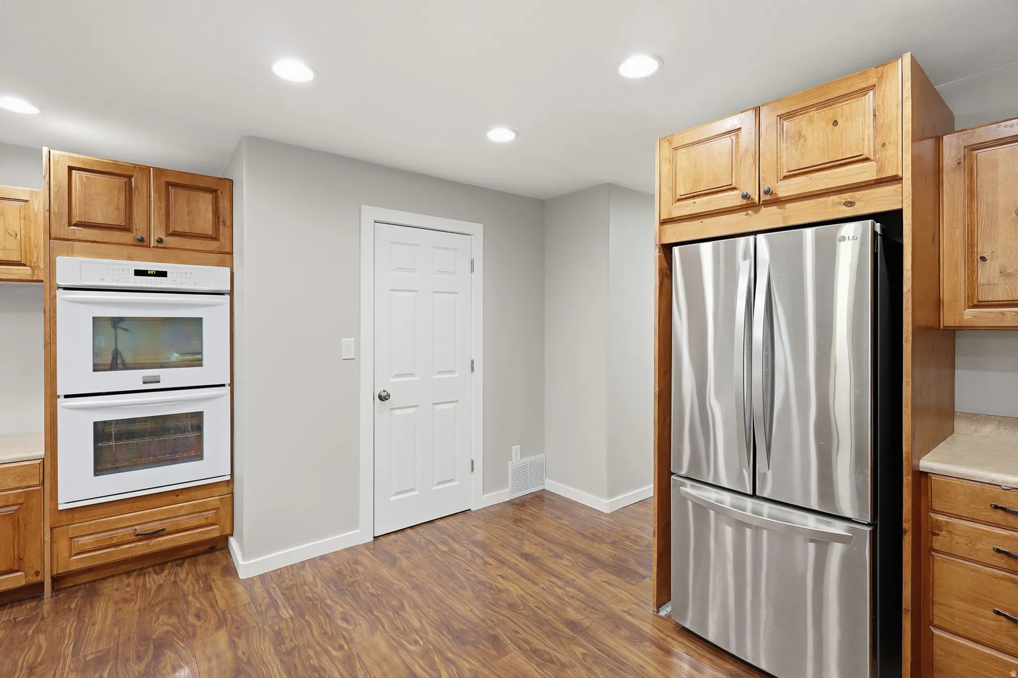 Stainless steel refrigerator, built-in double ovens, wood-finish cabinetry, recessed ceiling lighting, and wood-finish flooring