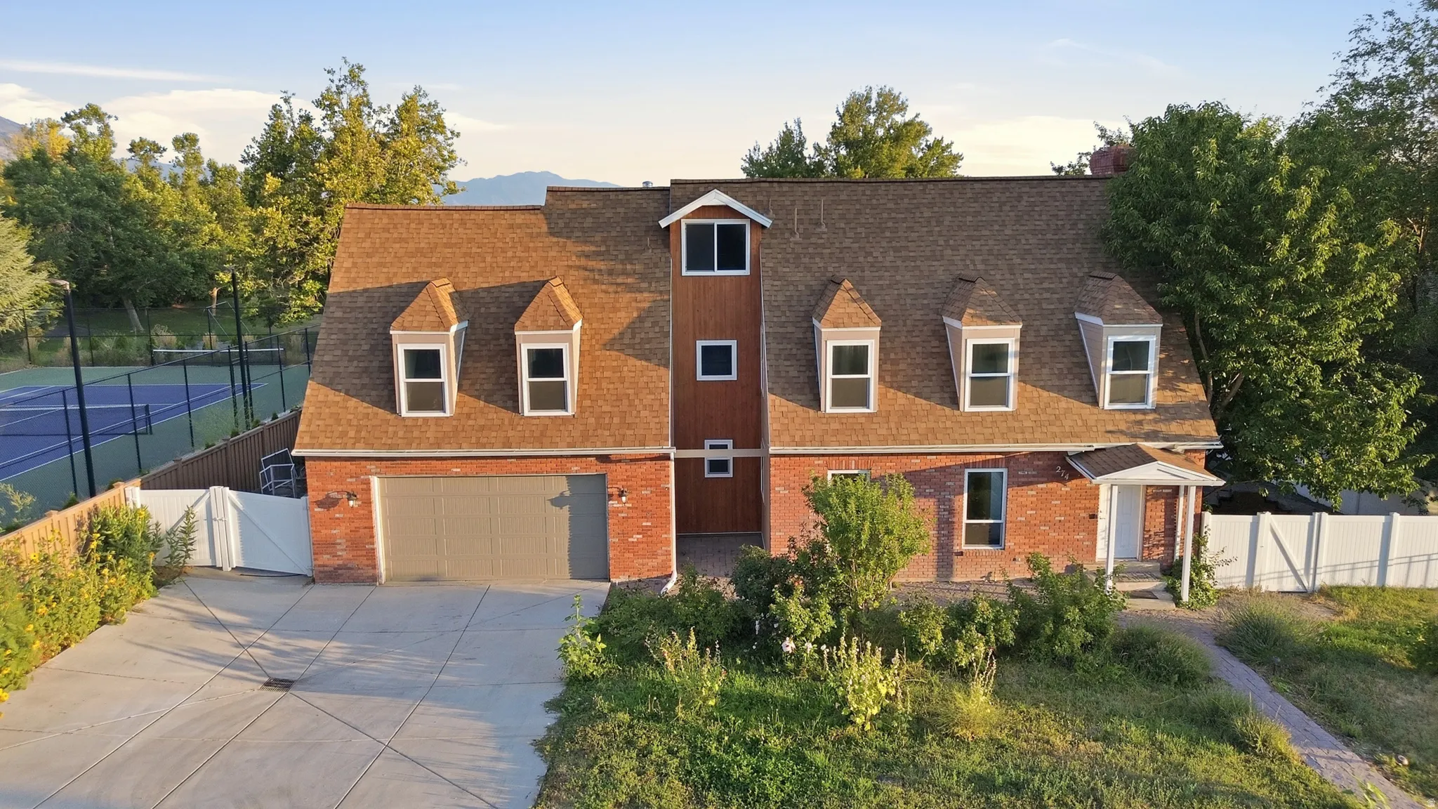 Brick exterior with dormer windows, attached garage, covered entry, and a dedicated tennis court