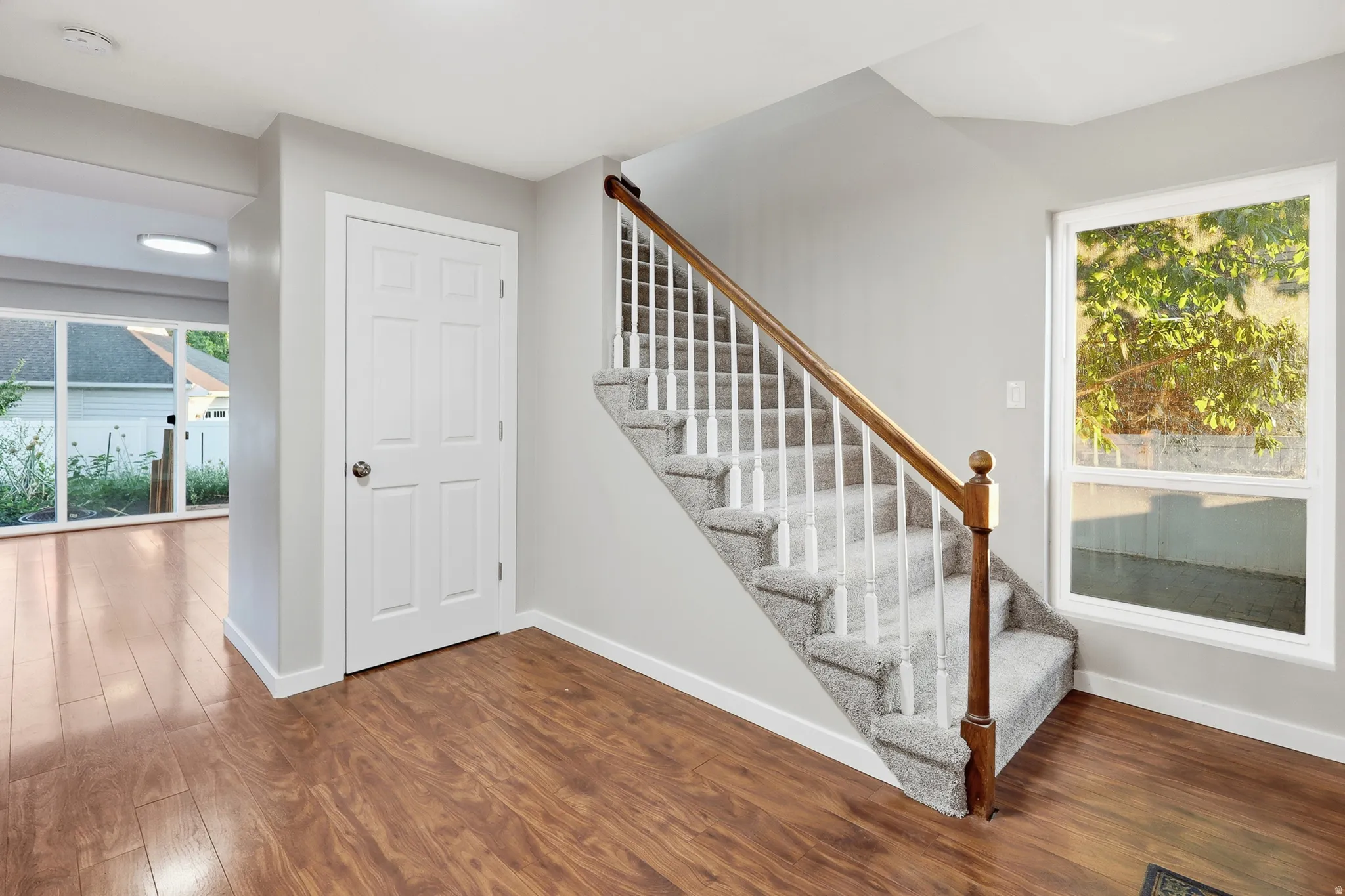 Wood-finish flooring throughout, carpeted staircase with wood handrail, and white paneled interior door