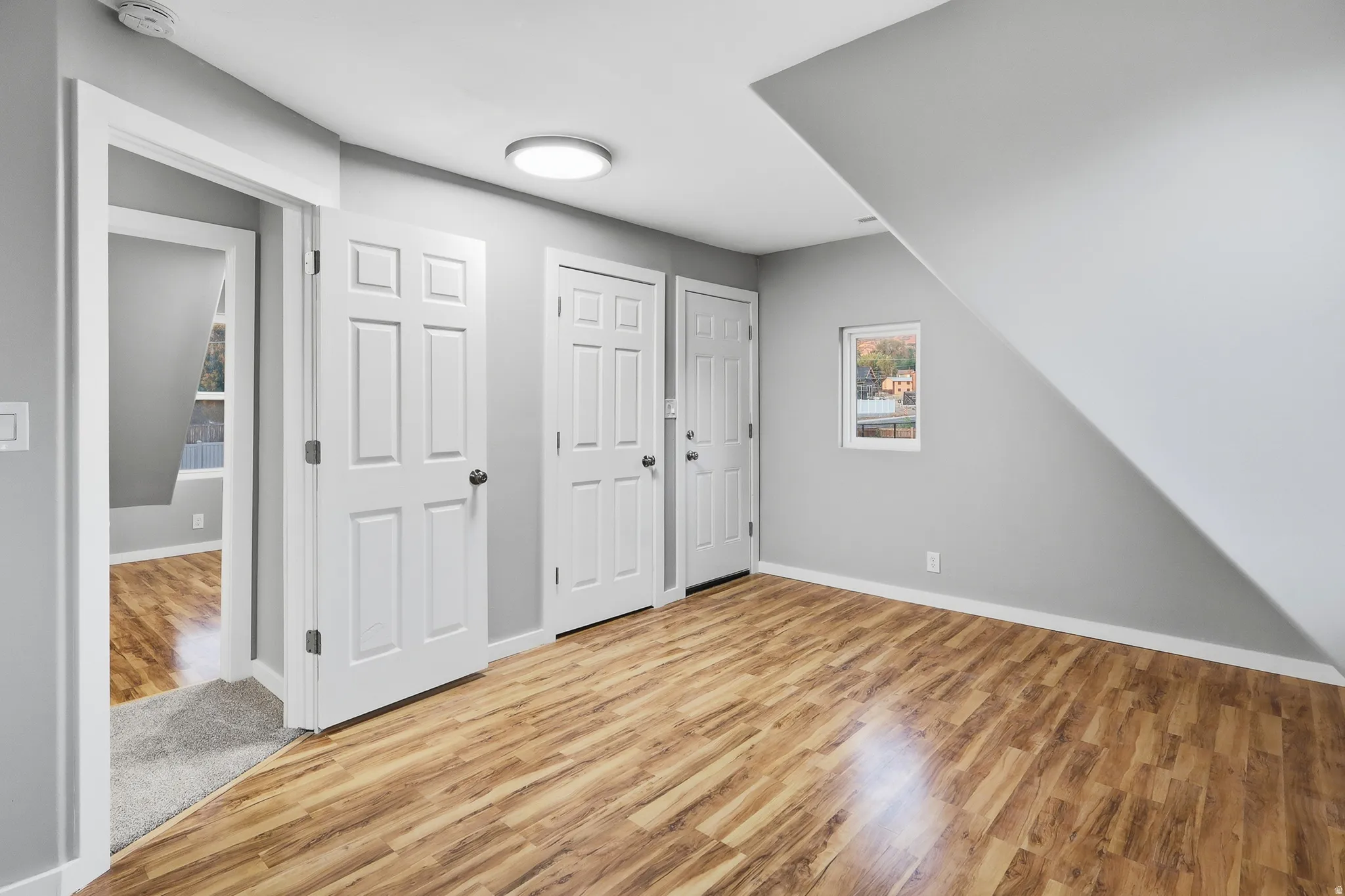 Wood-finish flooring with light gray walls, multiple paneled doors, and a ceiling-mounted light fixture
