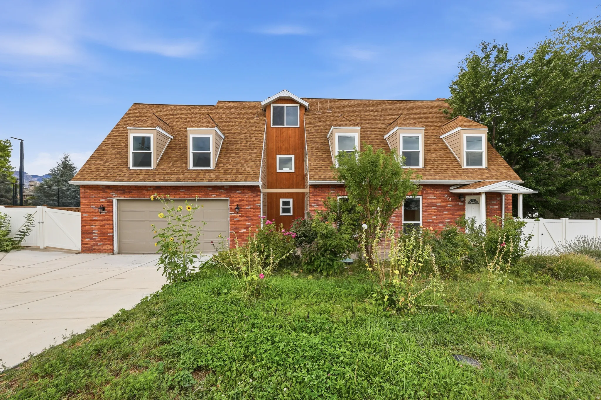 Brick exterior with a dormer roof, attached garage, and white perimeter fencing