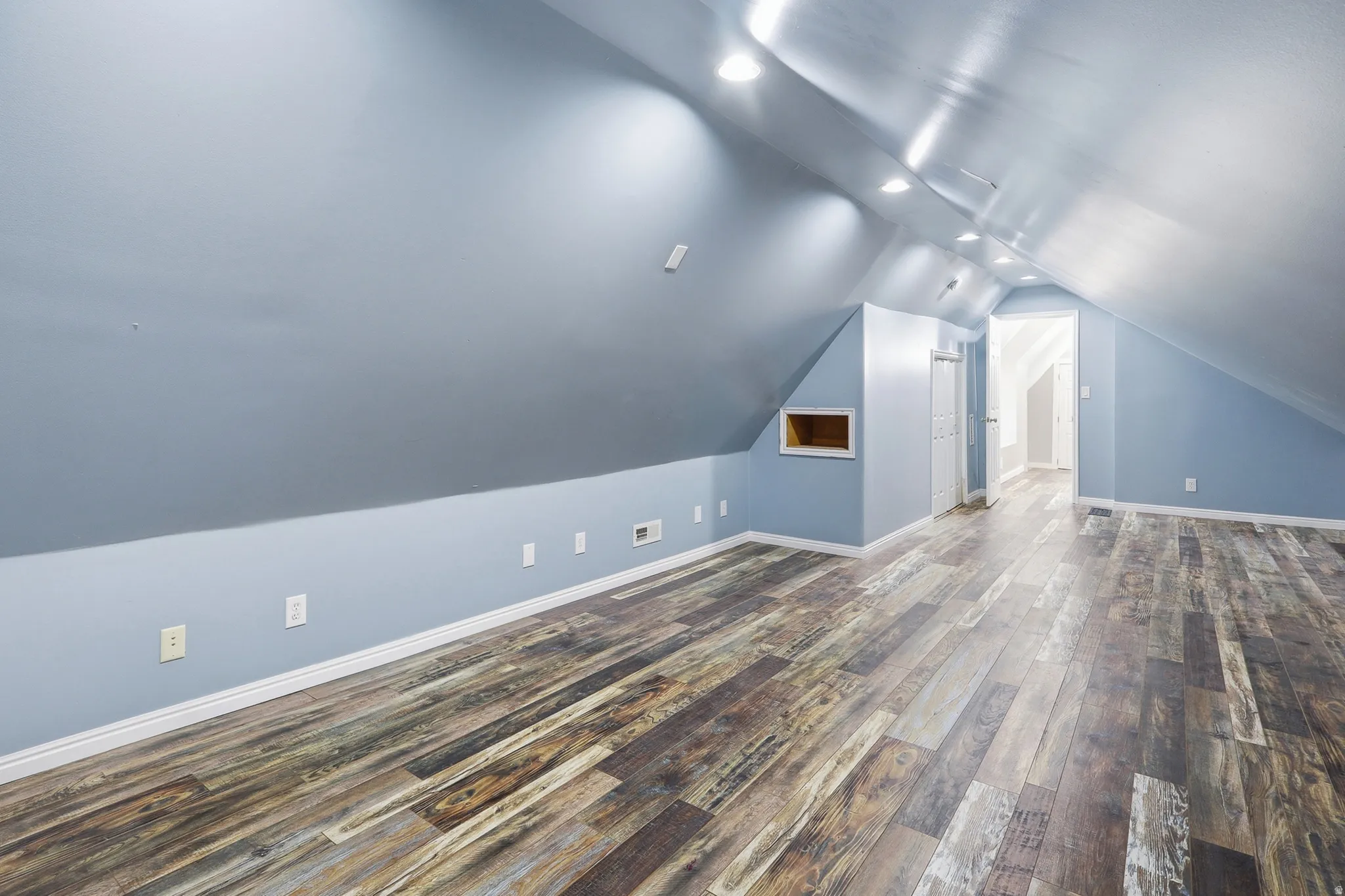 Wood-finish flooring, recessed ceiling lighting, vaulted ceiling, built-in wall niche, and doorway access