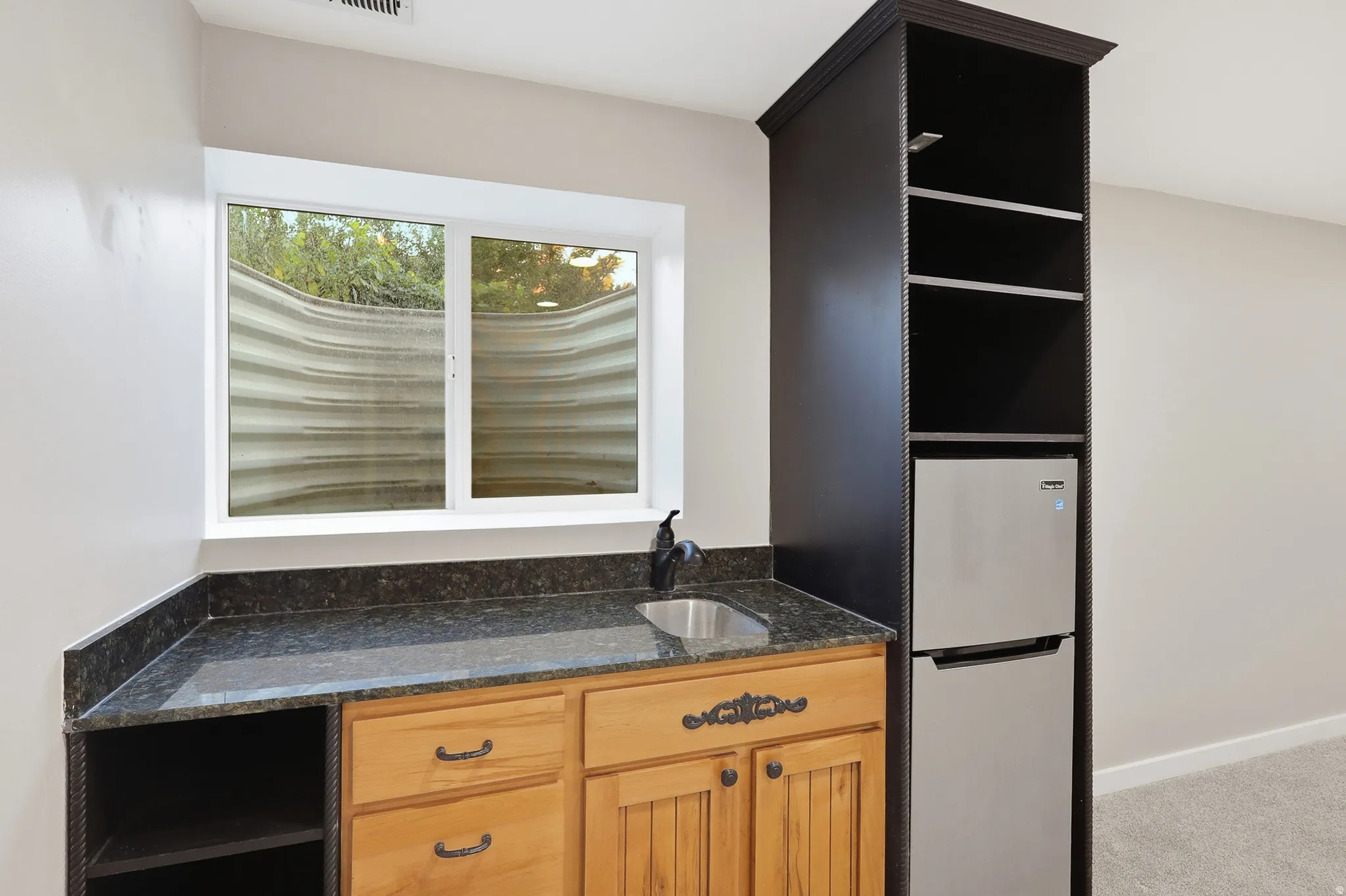 Built-in bar area featuring a stainless steel sink, dark-toned countertop, and light wood-finish cabinetry